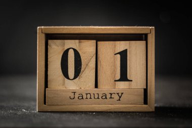 Tahta bloklardan oluşan takvime ait makro bir çekim. Siyah zemin üzerinde 1 Ocak tarihi var. Yeni yıl arifesi havası.