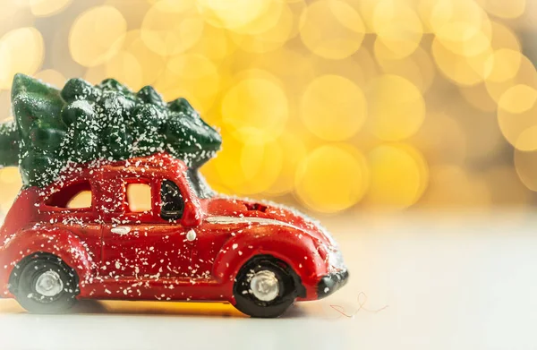 Retro red car delivering Christmas tree. Macro shot on the Christmas and New Year blurred background. Beautiful warm light bokeh. Merry Christmas mood.