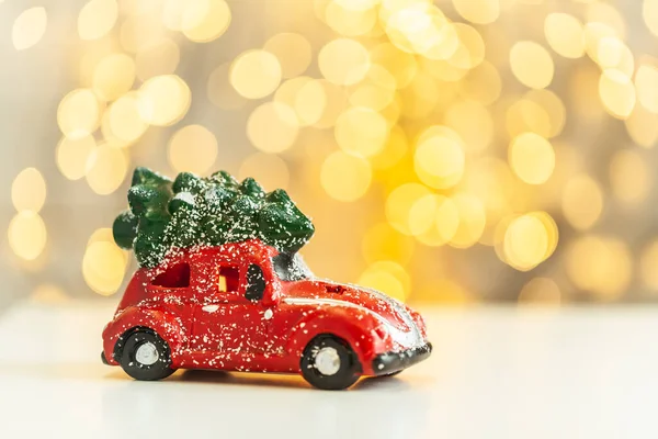 Retro red car delivering Christmas tree. Macro shot on the Christmas and New Year blurred background. Beautiful warm light bokeh. Merry Christmas mood.