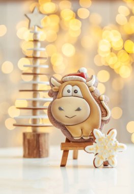 Boğa şekilli zencefilli kurabiye, arka plandaki ahşap tezgahta. Sıcacık Noel ışıkları. Yeni Yıl 'ın sembolü. Öküz yılı. Kış tatili ruhu