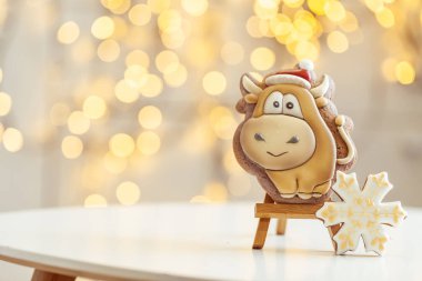 Boğa şekilli zencefilli kurabiye, arka plandaki ahşap tezgahta. Sıcacık Noel ışıkları. Yeni Yıl 'ın sembolü. Öküz yılı. Kış tatili ruhu