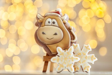 Boğa şekilli zencefilli kurabiye, arka plandaki ahşap tezgahta. Sıcacık Noel ışıkları. Yeni Yıl 'ın sembolü. Öküz yılı. Kış tatili ruhu