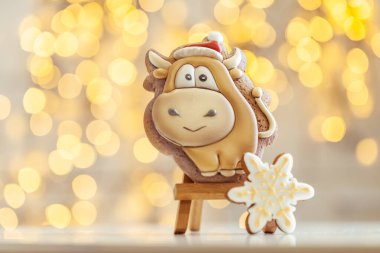 Boğa şekilli zencefilli kurabiye, arka plandaki ahşap tezgahta. Sıcacık Noel ışıkları. Yeni Yıl 'ın sembolü. Öküz yılı. Kış tatili ruhu