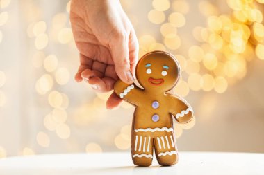 Bulanık Noel ışıkları arka planında zencefilli kurabiye. Sıcak bokeh ışıkları. Zencefilli kurabiye tutan bir kadının makro resmi. Yılbaşı ve kış tatili geçmişi. Kış kahve zamanı..