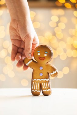 Bulanık Noel ışıkları arka planında zencefilli kurabiye. Sıcak bokeh ışıkları. Zencefilli kurabiye tutan bir kadının makro resmi. Yılbaşı ve kış tatili geçmişi. Kış kahve zamanı..