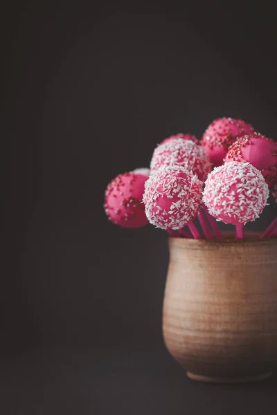 Pink chocolate cake pops in the rustic brown cup on the vintage dark background. Bisquit cake pops sprinkled with coconut flakes. St. Valentine\'s Day