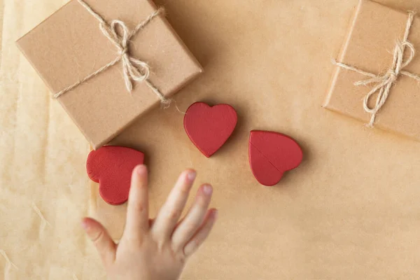 かわいい赤いハート型のおもちゃを持っている子供の手 茶色の再生紙の背景に段ボール箱にプレゼントや贈り物を提示します 平置きだ バレンタインデー — ストック写真