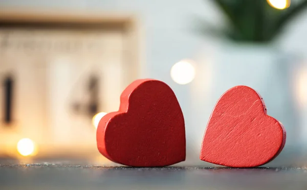 Two red hearts against the wooden calendar of blocks with the date of February 14 on the blurred dark concrete background. two red hearts with bokeh lights behind. Happy Valentine's day.