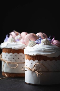 Paskalya pastası, beyaz şeker kreması, krema ve kurabiye ile süslenmiş tatlı ekmek. Kulich karanlık arka planda bir el işi kağıdına sarılmış..