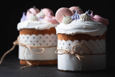 Paskalya pastası, beyaz şeker kreması, krema ve kurabiye ile süslenmiş tatlı ekmek. Kulich karanlık arka planda bir el işi kağıdına sarılmış..