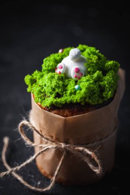 Paskalya pastası, yeşil çim şekeri ve tavşanla süslenmiş tatlı ekmek. Kulich karanlık arka planda bir el işi kağıdına sarılmış..
