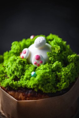 Paskalya pastası, yeşil çim şekeri ve tavşanla süslenmiş tatlı ekmek. Kulich karanlık arka planda bir el işi kağıdına sarılmış..