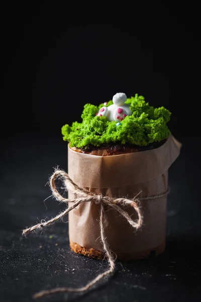 イースターケーキ 緑の草の砂糖アイシングとウサギで飾られた甘いパン 暗い背景にクラフト紙に包まれたクルチ — ストック写真