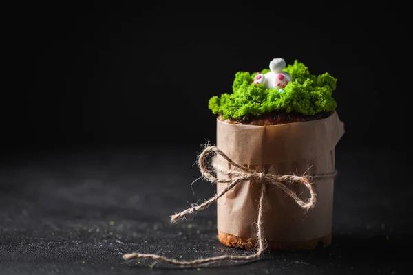 イースターケーキ 緑の草の砂糖アイシングとウサギで飾られた甘いパン 暗い背景にクラフト紙に包まれたクルチ — ストック写真