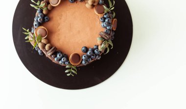 Beyaz arka planda yaban mersini, kurabiye ve çikolatayla süslenmiş çikolatalı pasta. Kahverengi doğum günü pastasının düzlüğü