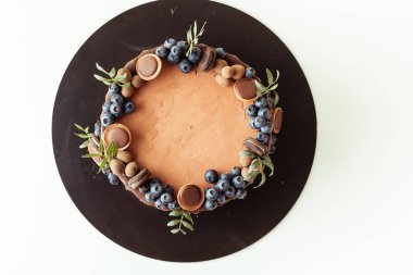 Beyaz arka planda yaban mersini, kurabiye ve çikolatayla süslenmiş çikolatalı pasta. Kahverengi doğum günü pastasının düzlüğü