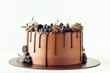 Beyaz arka planda yaban mersini, kurabiye ve çikolatayla süslenmiş çikolatalı pasta. Kahverengi doğum günü pastasının düzlüğü