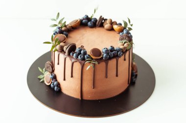 Beyaz arka planda yaban mersini, kurabiye ve çikolatayla süslenmiş çikolatalı pasta. Kahverengi doğum günü pastasının düzlüğü