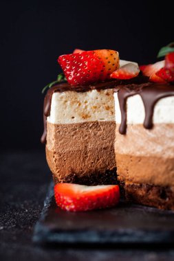 Siyah arka planda çikolata damlayan üç çikolatalı pasta. Sütlü, üstünde çilek desenli siyah beyaz çikolatalı pasta. Kopya alanı olan şekerleme arkaplanı