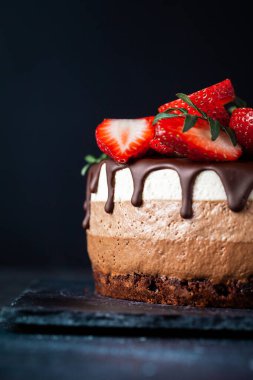 Siyah arka planda çikolata damlayan üç çikolatalı pasta. Sütlü, üstünde çilek desenli siyah beyaz çikolatalı pasta. Kopya alanı olan şekerleme arkaplanı