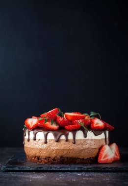 Siyah arka planda çikolata damlayan üç çikolatalı pasta. Sütlü, üstünde çilek desenli siyah beyaz çikolatalı pasta. Kopya alanı olan şekerleme arkaplanı