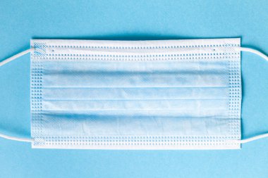 Açık mavi arka planda mavi cerrahi maske. Coronavirus Covid-19 'a karşı tek kullanımlık maske. Gribe karşı koruma, solunum virüsü, hava kirliliği. Virüs salgını sırasında sağlık sigortası. Düz yatıyordu