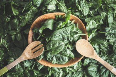 Ispanaklı marul salatası. Koyu yeşil arka plan. Ahşap kasedeki yeşil yaprakları ahşap çatal bıçakla kapatın. Düz yatıyordu