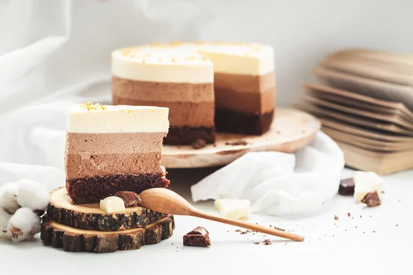 Three layered chocolate mousse cake on the wooden stand on white background. Good morning with fresh coffee and chocolate souffle cake. Vintage background