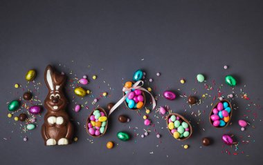 Çikolatalı Paskalya yumurtaları ve içi şekerle dolu tavşan tavşanı, gri arka planda renkli şekerlerle çevrili. Paskalya arkaplanı.