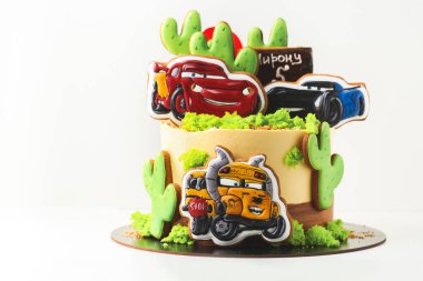 KYIV, UKRAINE - 3 Mart: Sarı krem peynirli doğum günü pastası üzerinde zencefilli kurabiyeler ile süslenmiş Arabalar çizgi film karakterleri ve çöl manzarası küçük bir çocuk için beyaz arka plan