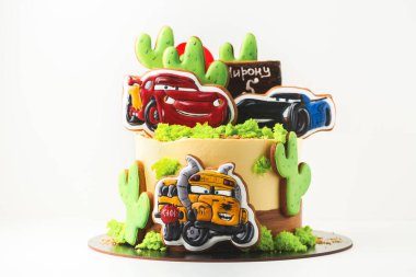 KYIV, UKRAINE - 3 Mart: Sarı krem peynirli doğum günü pastası üzerinde zencefilli kurabiyeler ile süslenmiş Arabalar çizgi film karakterleri ve çöl manzarası küçük bir çocuk için beyaz arka plan