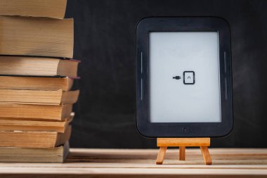 E-kitap okuyucu, siyah arka plandaki kağıt yığınının yanındaki ahşap tezgahta. Elektronik okuma aygıtı sıradan kitaba karşı