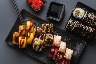 Suşi, somon, avokado ve yosunla sarılmış ton balığı. Suşi seti siyah arka planda siyah çubuklu kırmızı zencefilin yanındaki siyah tabakta servis ediliyor. Düz yatıyordu