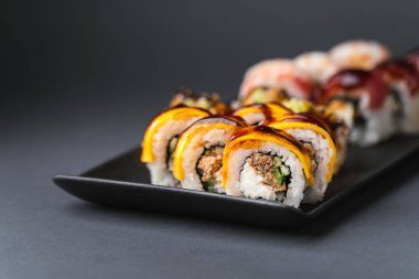 Somon, avokado ve ton balıklı suşi. Suşi seti siyah arkaplanda siyah çubuklu kırmızı zencefilin yanında servis edilir.
