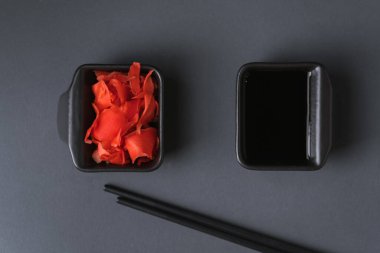 Suşi seti siyah arka planda siyah çubuklu kırmızı zencefilin yanındaki siyah tabakta servis ediliyor. Düz yatıyordu