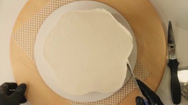 Pasta şefinin pasta tezgahını krem peynirle süslediği pasta poşeti ve spatulayla kapatmasını. Şekerlemecinin pastayı birleştirip süsleme süreci