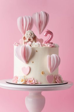 Güzel bir doğum günü pastası, pembe arka planda sevimli bir tavşancık figürü olan 2 yaşındaki küçük bir kız bebek için.
