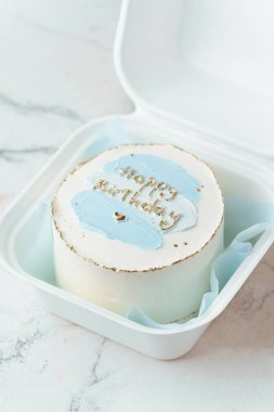 Küçük şirin bento pastası. Mutlu yıllar mesajı ve beyaz mermer arka plandaki beyaz hediye kutusunda mavi krema lekeleri.
