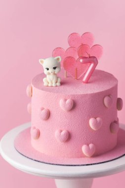 Çikolata kalpli ve şirin kedi yavrusu heykelciğiyle süslenmiş yedi yaşındaki bir kız için güzel bir doğum günü pastası. Pembe arkaplan