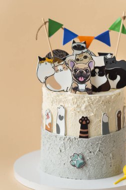 Bej arka planda yenilebilir köpek ve kedi figürleriyle süslenmiş güzel büyük bir doğum günü pastası. Küçük bir köpek ve kedi sever için kek.
