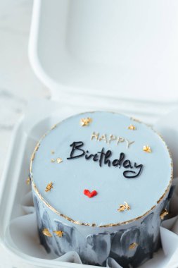 Beyaz arka planda beyaz bir hediye kutusunda küçük bir Kore tarzı mavi bento pastası. Üstünde Mutlu Yıllar metni olan pasta.