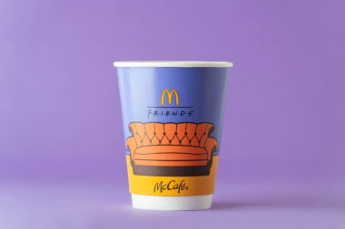 Kyiv, Ukrayna - 23 Aralık 2025: McDonalds kağıt kahve fincanı üzerinde Friends temalı bir tasarım ve mor arka planda koleksiyonluk karakter figürleri sergilenmektedir. Markalı logolar ve telif hakkı olan unsurlar görünür. Sadece editör kullanımı.