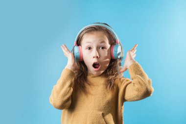 Şirin, küçük beyaz kız, kulaklık takan havalı sesten bunalmış. Mavi arka planda kulaklıkla müzik dinleyen mutlu küçük kız portresi.