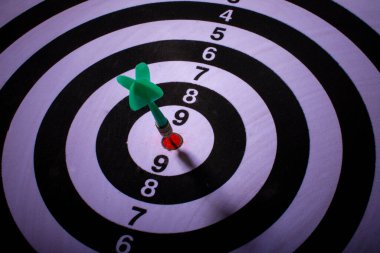 Siyah ve beyaz hedefin ortasına yeşil dart iğnesi saplanmış. Seçici odak.