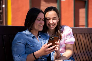 Güzel lezbiyen çift sokakta birbirlerini seviyorlar. Telefonla fotoğraf çekiyorlar ve gülüyorlar. Gururla yürüyorlar.