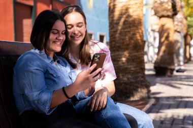 Güzel lezbiyen çift sokakta birbirlerini seviyorlar, telefonla fotoğraf çekiyorlar, gülüyorlar ve LGBT onur bayrağıyla yürüyorlar.