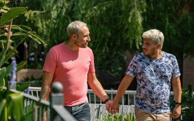 İki genç adam parkta yürür, sever, sarılırlar ve manzaraya bakarlar.