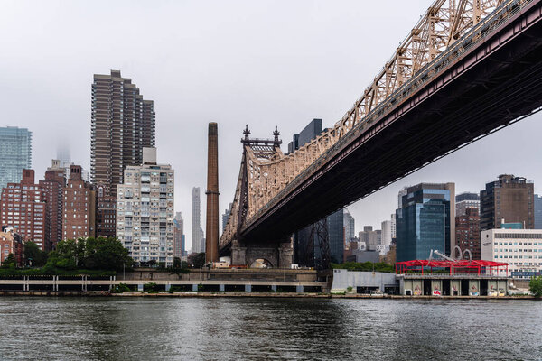 New York City, USA - June 24, 2018: View under Queensboro Bridge, Roosevelt Island Tramway and skyline of Upper East Side of Manhattan. Foggy day in NYC over East River