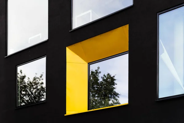 Gelbes Fenster auf schwarzer Fassade mit Reflexion des grünen Baumes auf. — Stockfoto