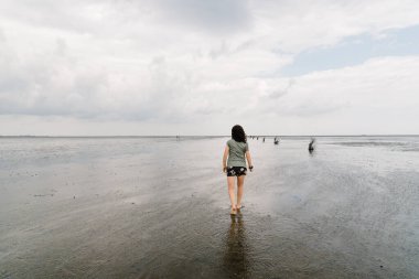 Genç bir kadın sakin ve sakin bir sahilde tek başına yürüyor.